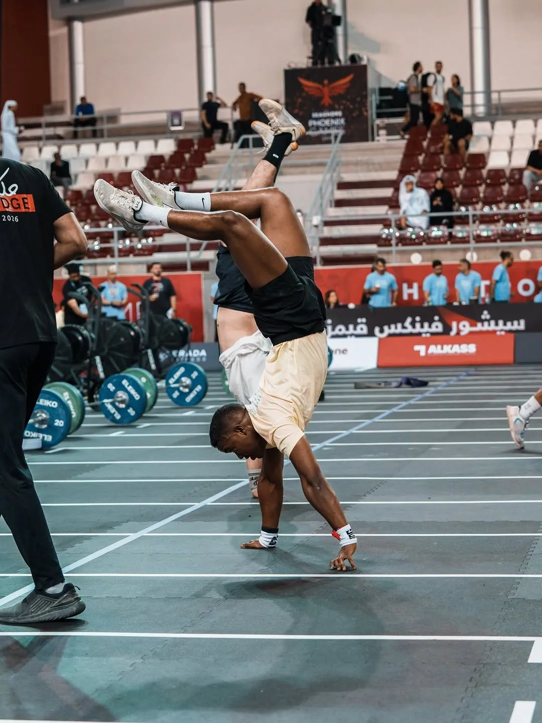 Wide view of an indoor arena during a handstand walk, bumper plates on the floor